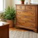 An antique wooden chest of drawers in a cozy, sunlit room, with a fern and a white bowl of baking soda on an adjacent table.