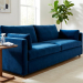 A deep sapphire blue velvet sofa in a bright modern living room. A side table holds a cleaning brush, microfiber cloth, and spray bottle.